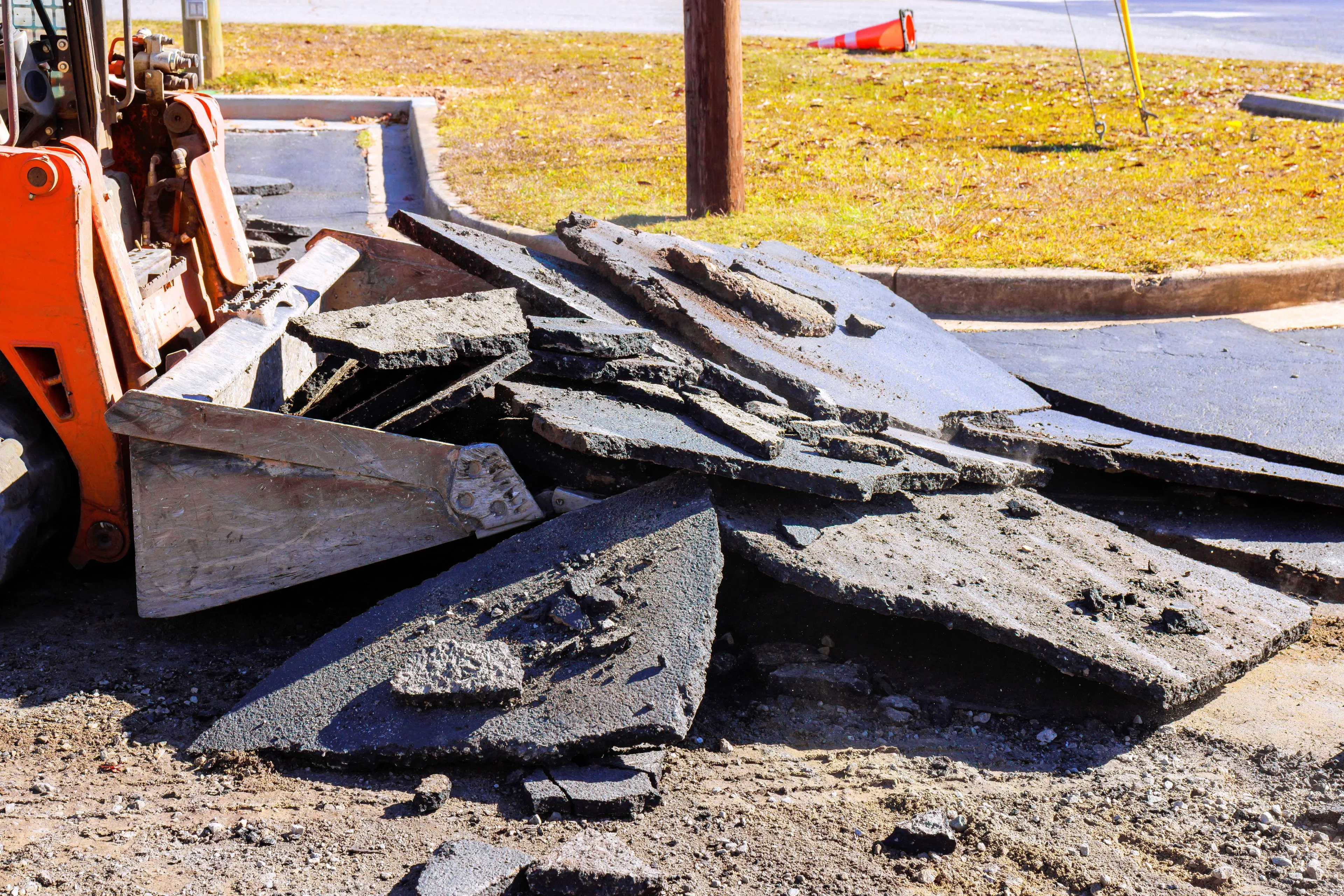A heavy-duty skid steer loader lifting and removing large layers of broken asphalt from a parking lot project in Dallas, managed by DALLAS DEMO PROS.