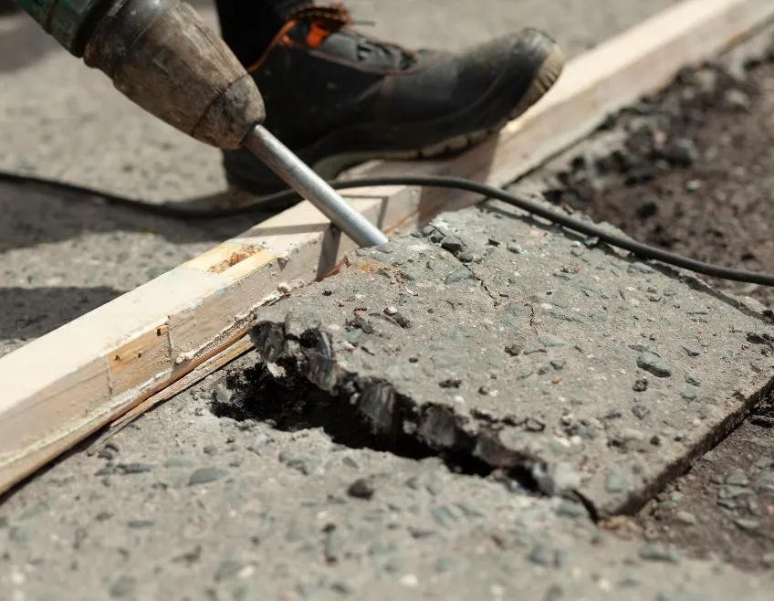 Hydraulic breaker machine demolishing a thick concrete slab for a residential removal project in Dallas.