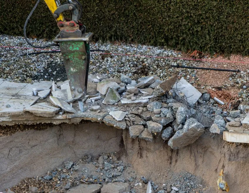 Professional heavy machinery breaking concrete during a swimming pool removal and ground leveling project in Dallas